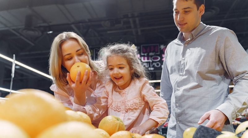 Family enjoying a cheerful shopping trip together at the grocery store, selecting fresh oranges.
